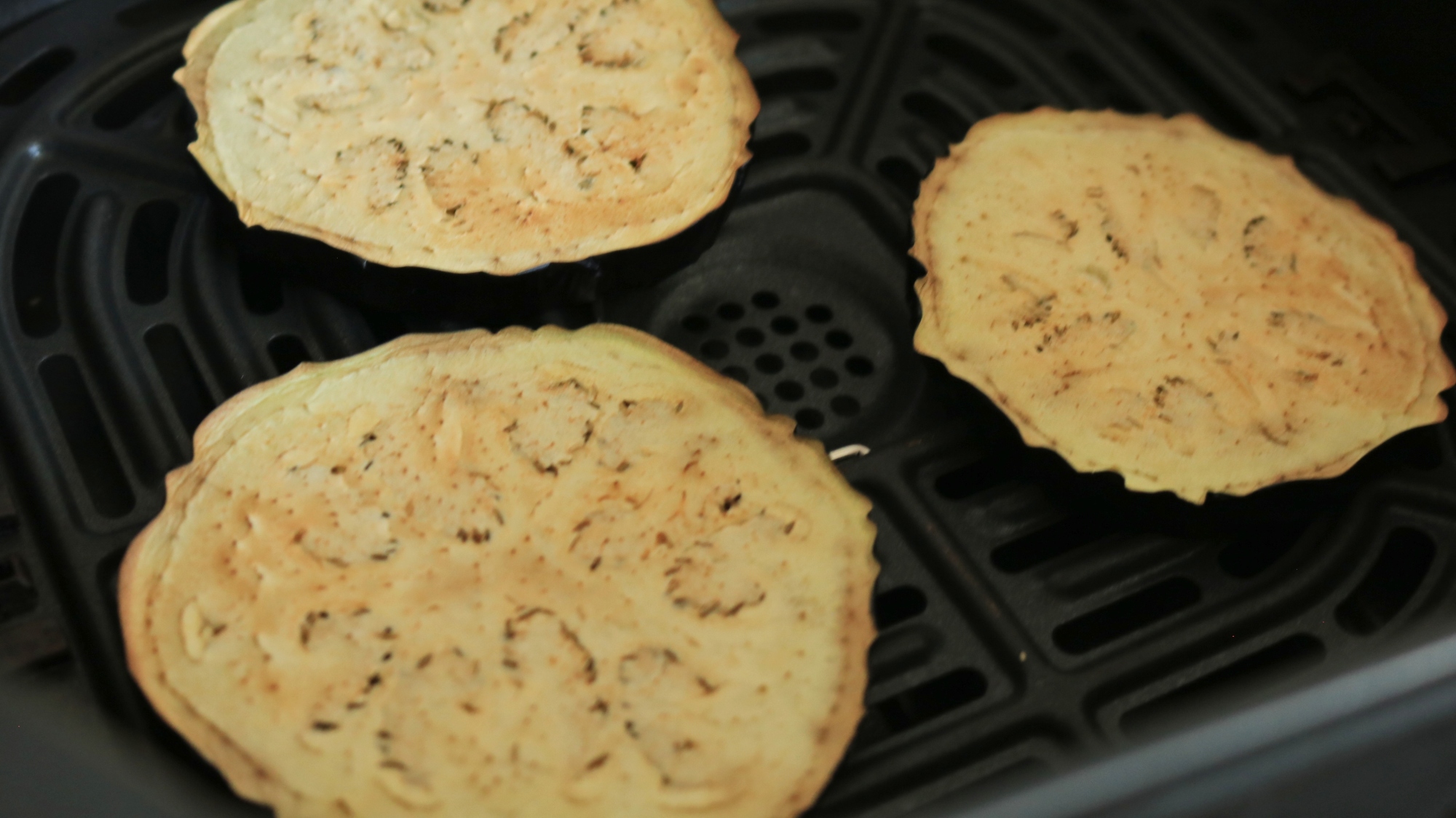 Slices of eggplant in an air fryer basket.