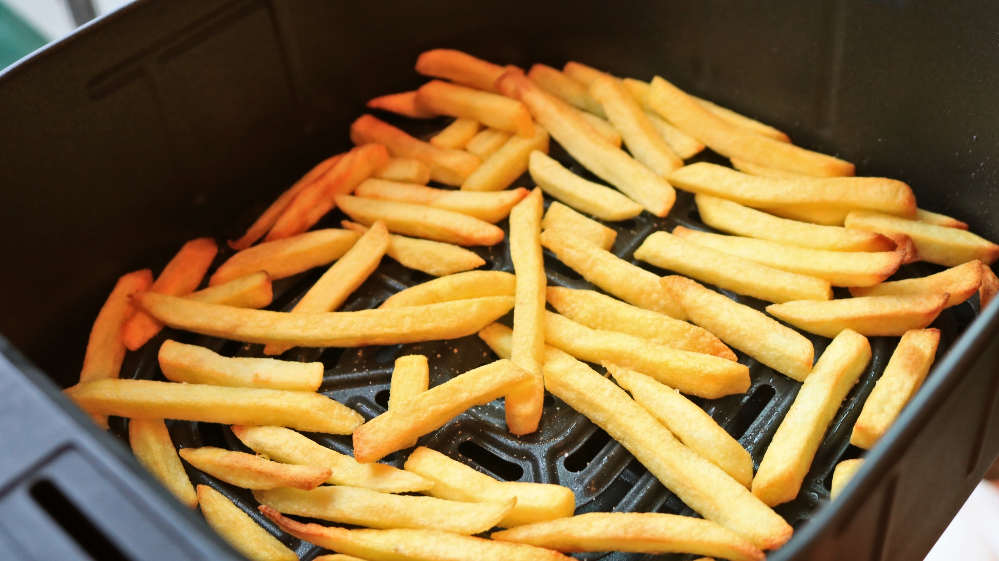 Reheated french fries in an air fryer basket.