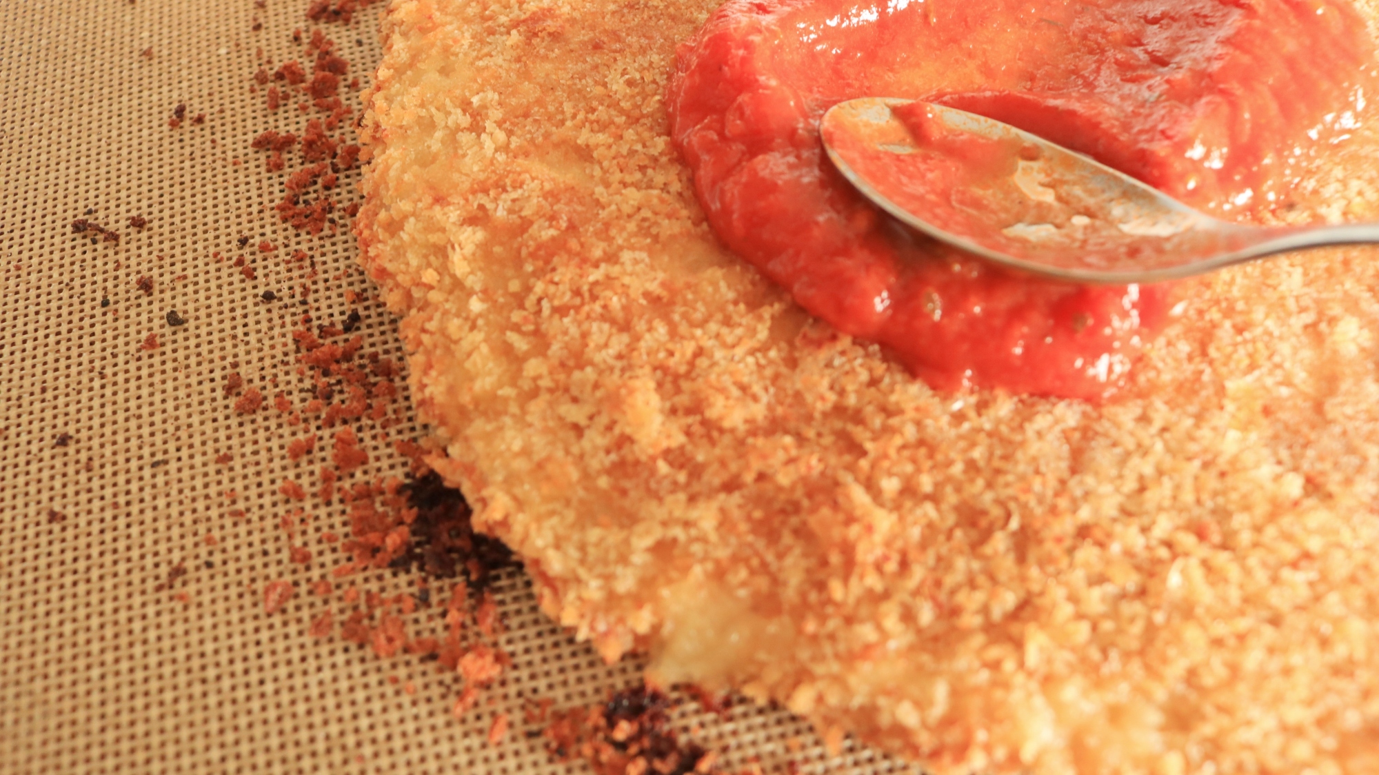 Spoon spreading tomato sauce on a chicken crust.