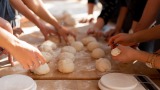 Hands placing bread dough on a cutting board in culinary class.